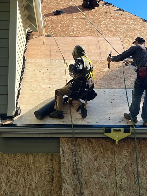 Roofers in full safety gear on a steep roof